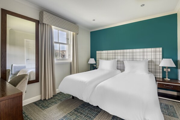 Una habitación de hotel con una cama grande, dos mesitas de noche, un espejo, una ventana con cortinas y una pared de acento color turquesa.
