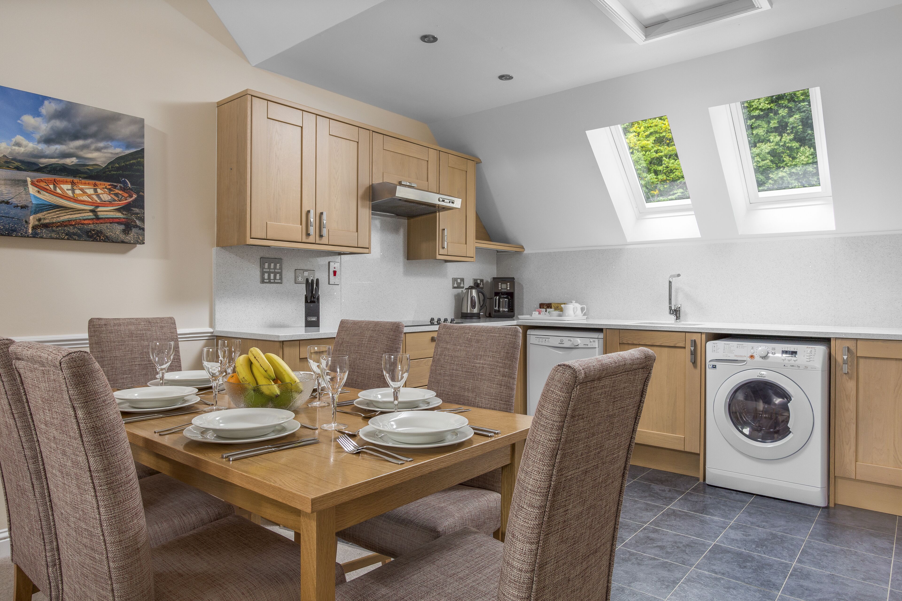 A modern kitchen with wooden cabinets, a dining table set for six, and a washing machine.