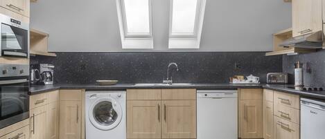 A modern kitchen with built-in appliances, a washing machine, and a dishwasher.