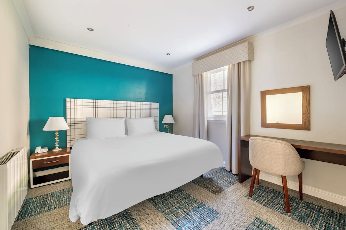 A hotel room with a large bed, a desk, and a chair.