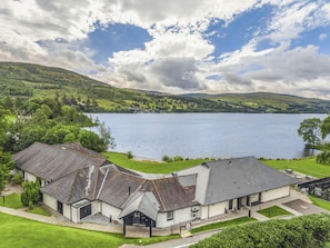 A lakeside building with a reception area, surrounded by lush greenery and a large body of water. - The Kenmore Club (Aberfeldy)