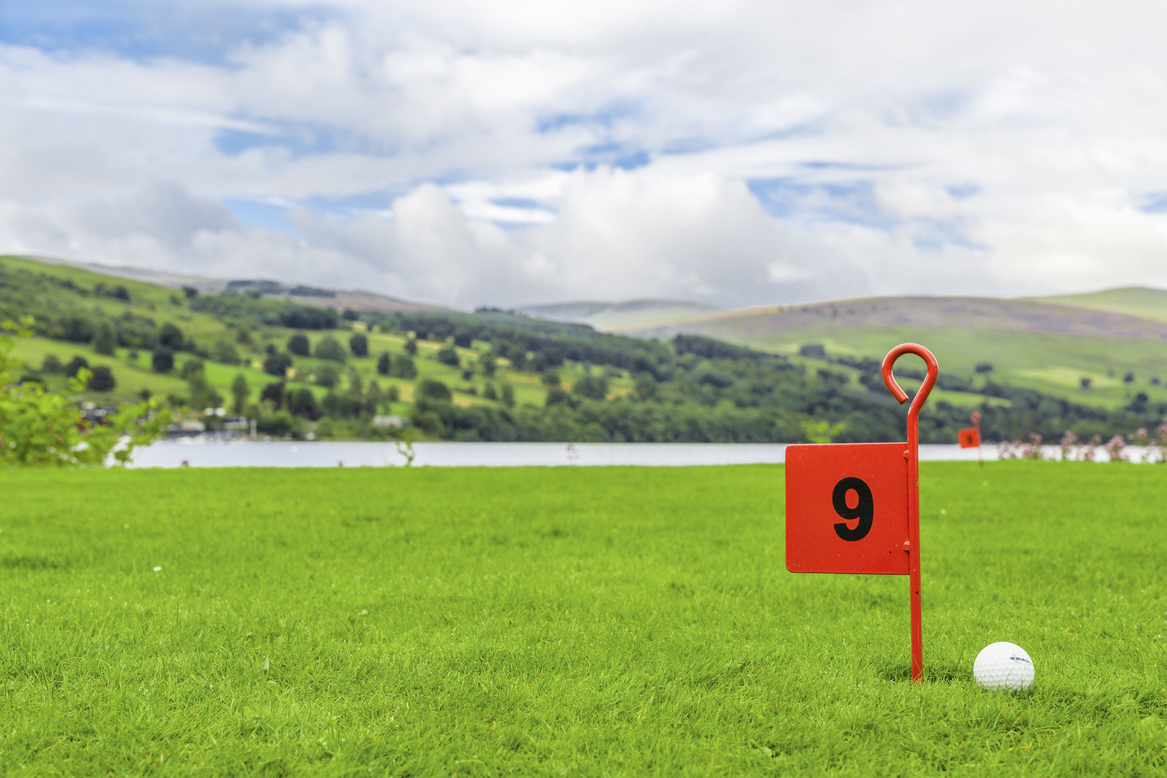 Un campo de golf con una bandera roja marcada con el número 9 y una pelota de golf sobre el césped.