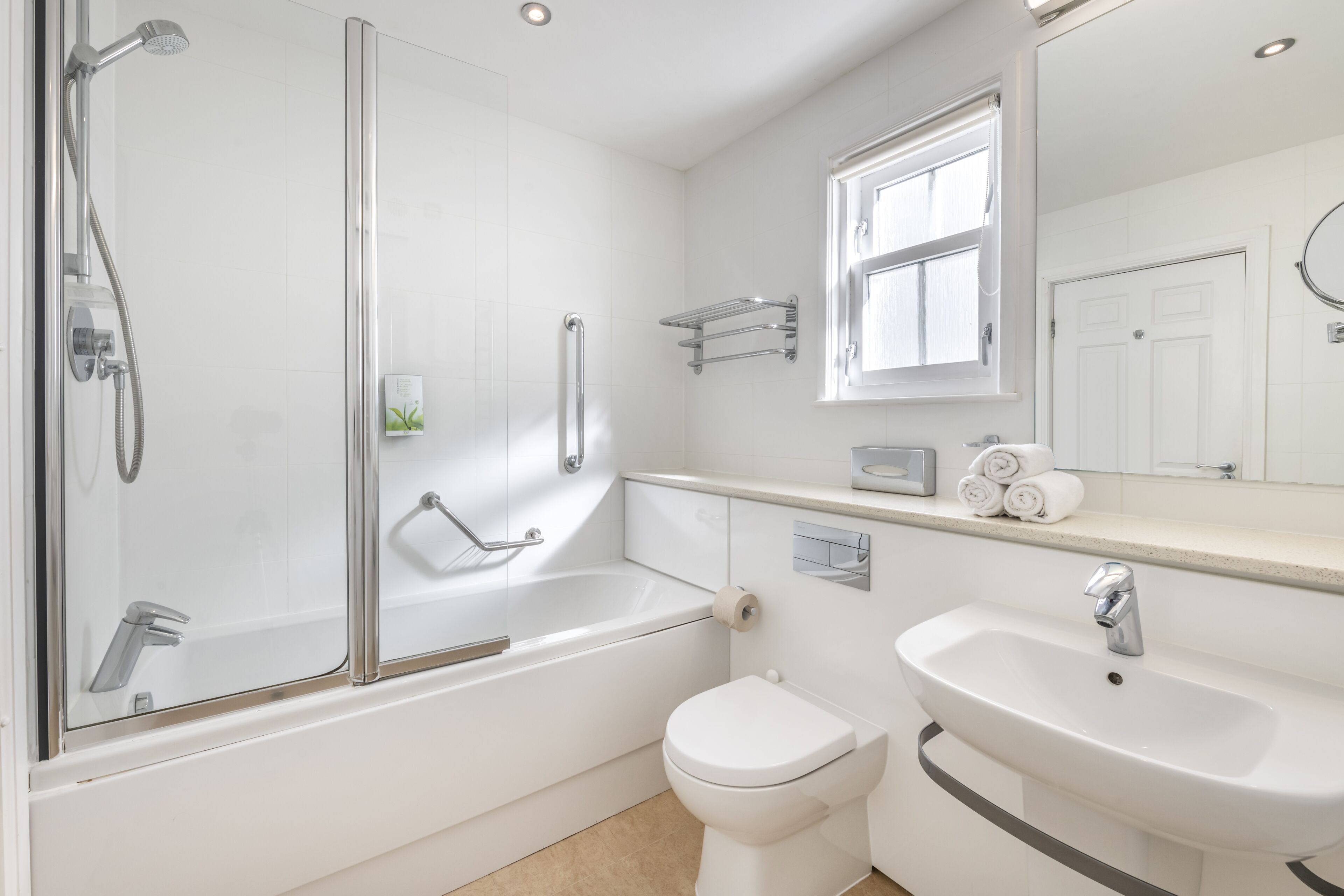 A modern bathroom with a glass-enclosed shower, a white bathtub, a toilet, and a sink.