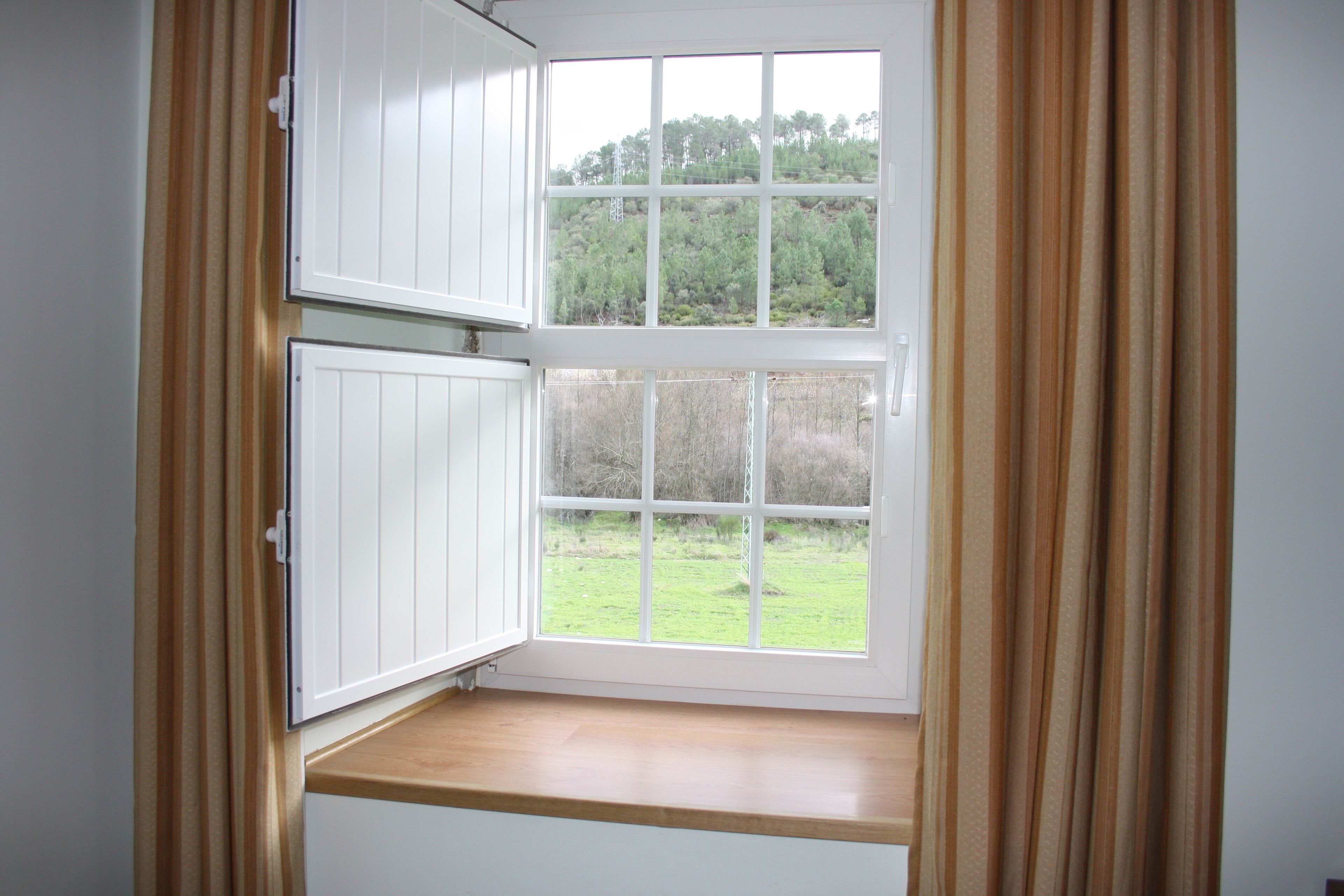 Ein Zimmer mit großem Fenster, einer Holzbank und Blick auf eine grüne Landschaft.