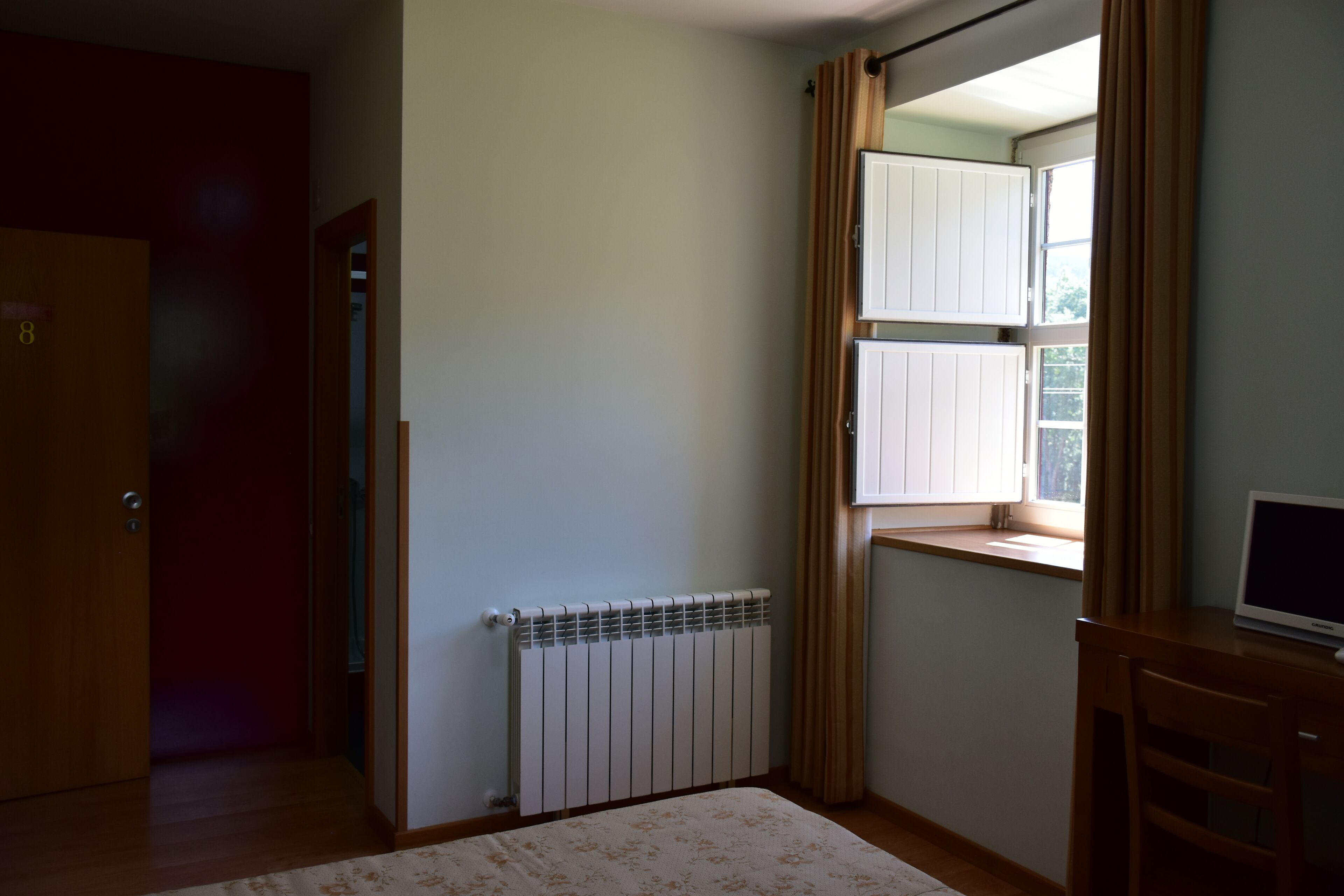 A room with a radiator, a wooden door, a window with curtains, and a desk with a computer.