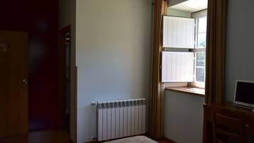 A room with a radiator, a wooden door, a window with curtains, and a desk with a computer.