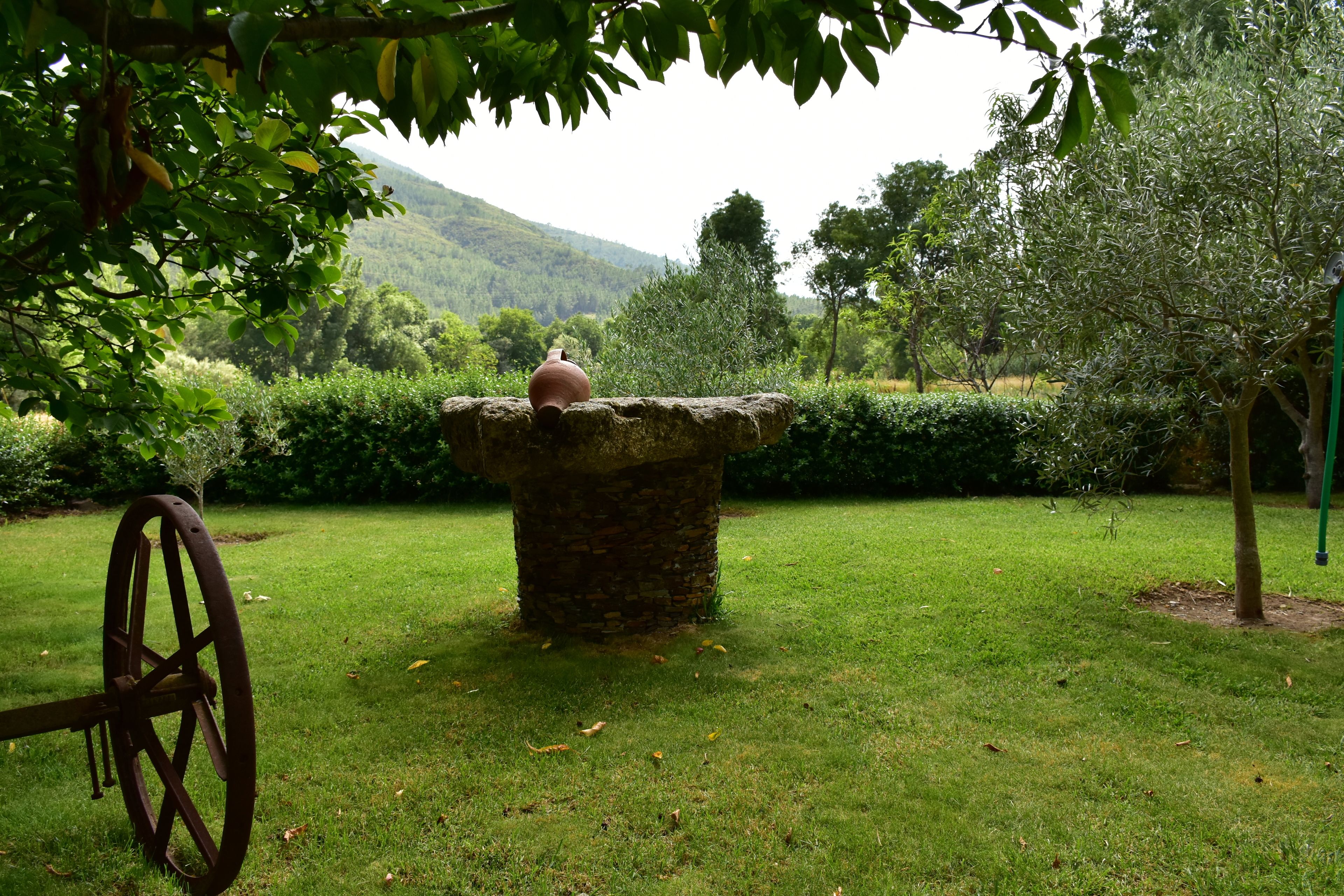 A stone table with a vase in a grassy garden with trees and hills in the background.