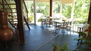 Een ruime binnenruimte met een groot koperen distillatie-apparaat, een trap en een eethoek met tafels en stoelen.