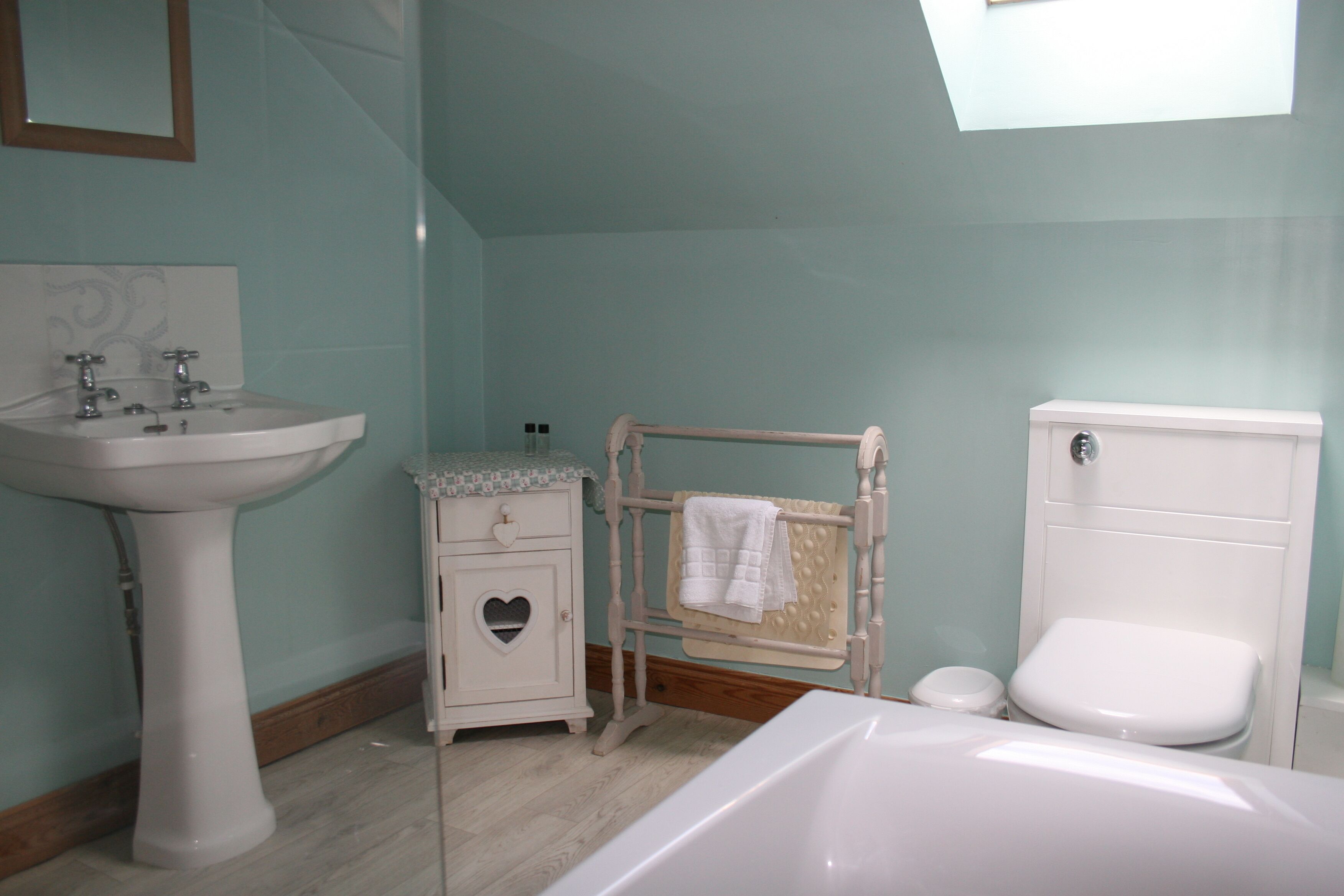 A bathroom with a white sink, a white toilet, a wooden towel rack, and a small cabinet with a heart-shaped cutout.
