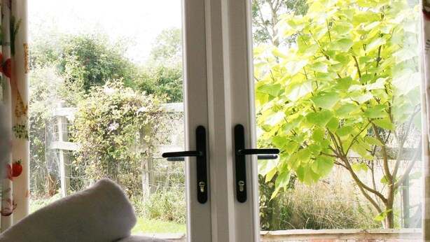 A room with a bed, a window with a view of greenery outside, and a rolled-up towel on the bed. - Broccoli Bottom (Oakham)