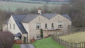 A stone house with a sloped roof, a paved driveway, and a wooden fence. - Broccoli Bottom (Oakham)