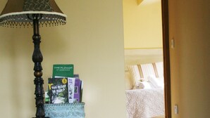 A room with a lamp, a small table with decorative items, a bed with a white bedspread, and a door leading to another room. - Broccoli Bottom (Oakham)