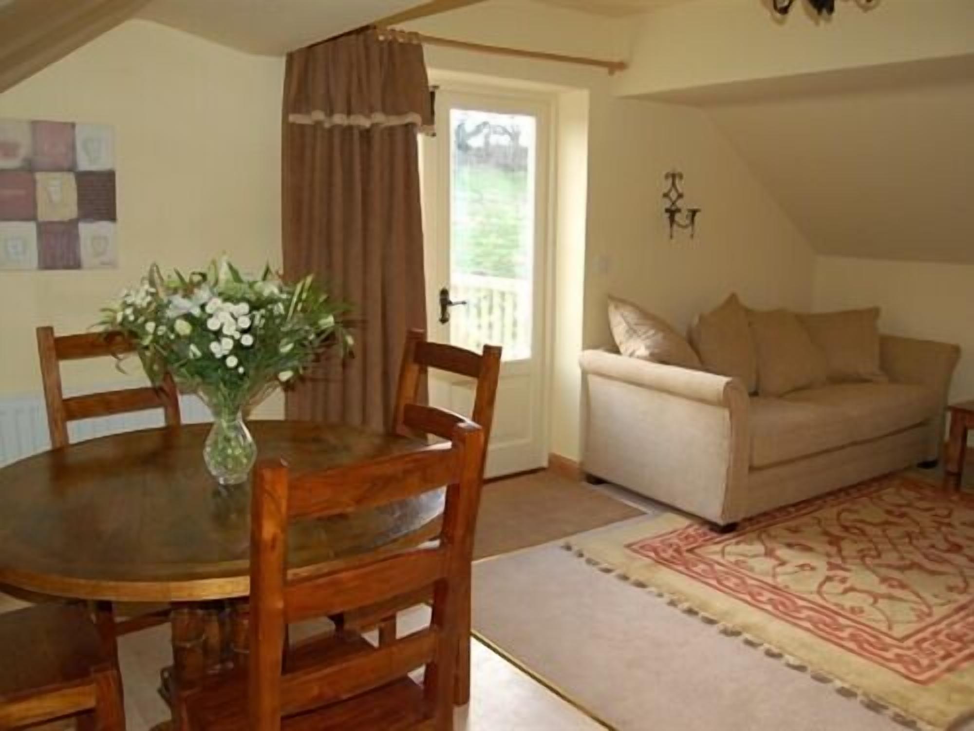 A cozy living room with a round wooden table, a beige sofa, and a patterned rug.