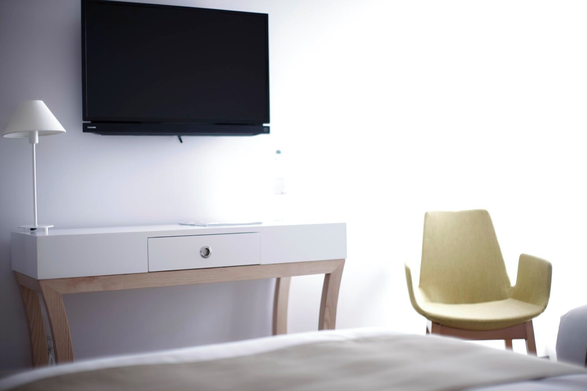 A hotel room with a bed, a desk with a lamp, a TV, and a chair.