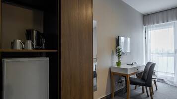 A hotel room with a kitchenette, a dining area with a table and chairs, a TV mounted on the wall, and a large window with curtains.