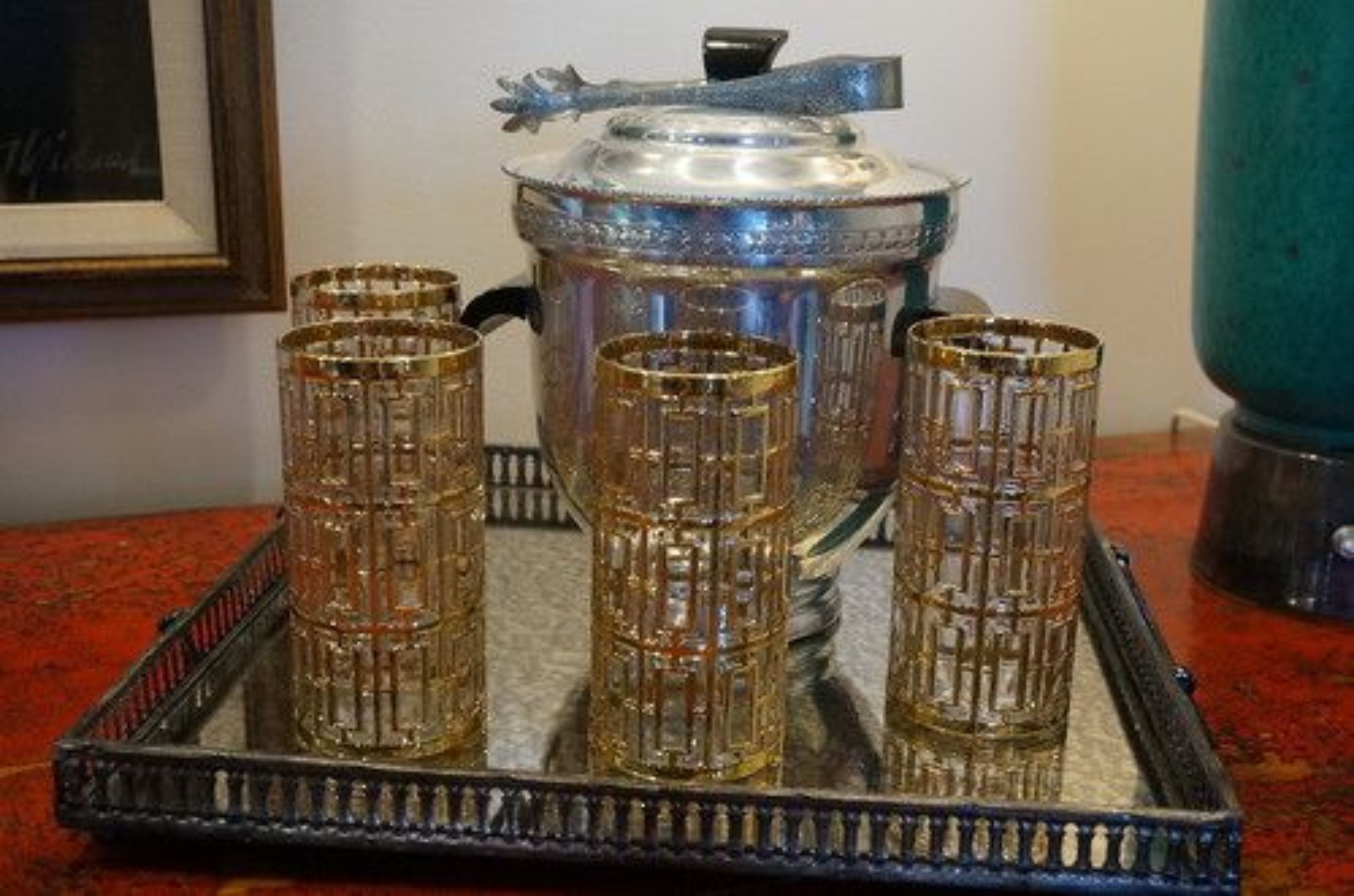 A tray with four glass tumblers and a silver pot on a red surface.