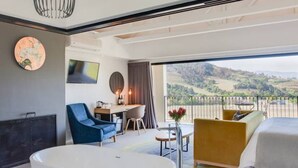 Quarto de hotel moderno com uma banheira grande, uma escrivaninha, uma cadeira azul, um sofá amarelo e uma janela ampla com vista para o campo.
