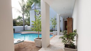 Uma área externa coberta com piscina, plantas em vasos e um banco.