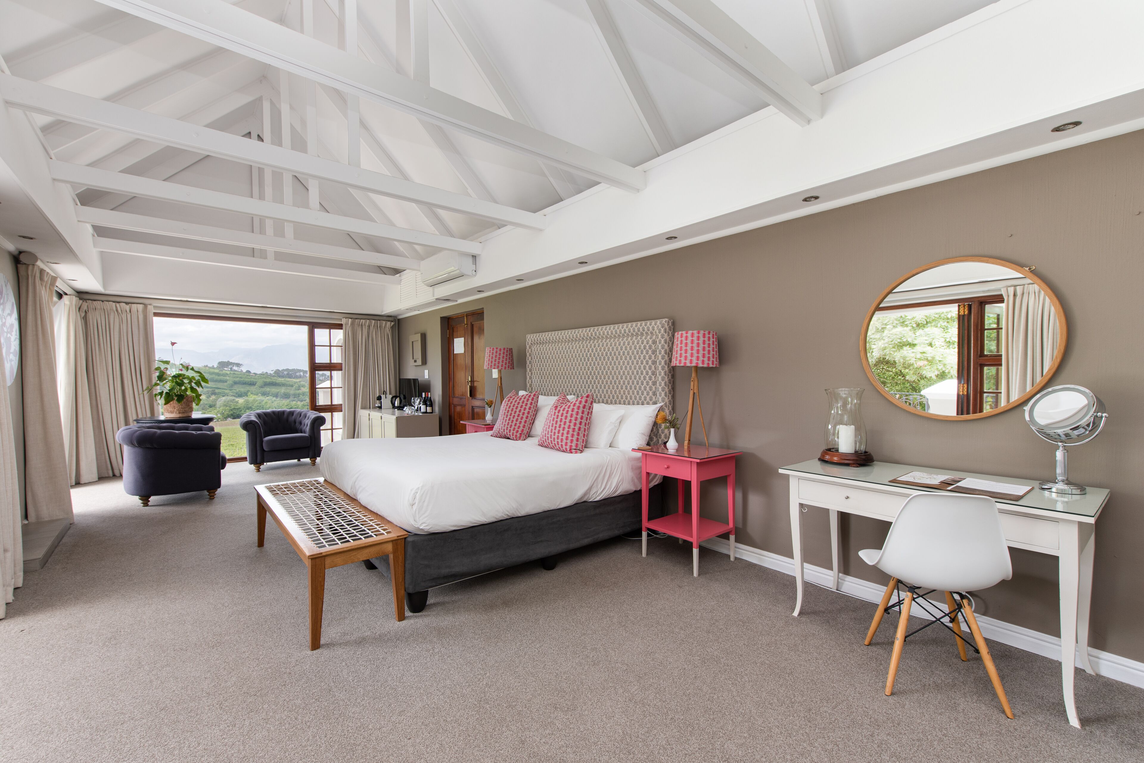 A bedroom with a bed, bedside table, chair, desk, and a large window.