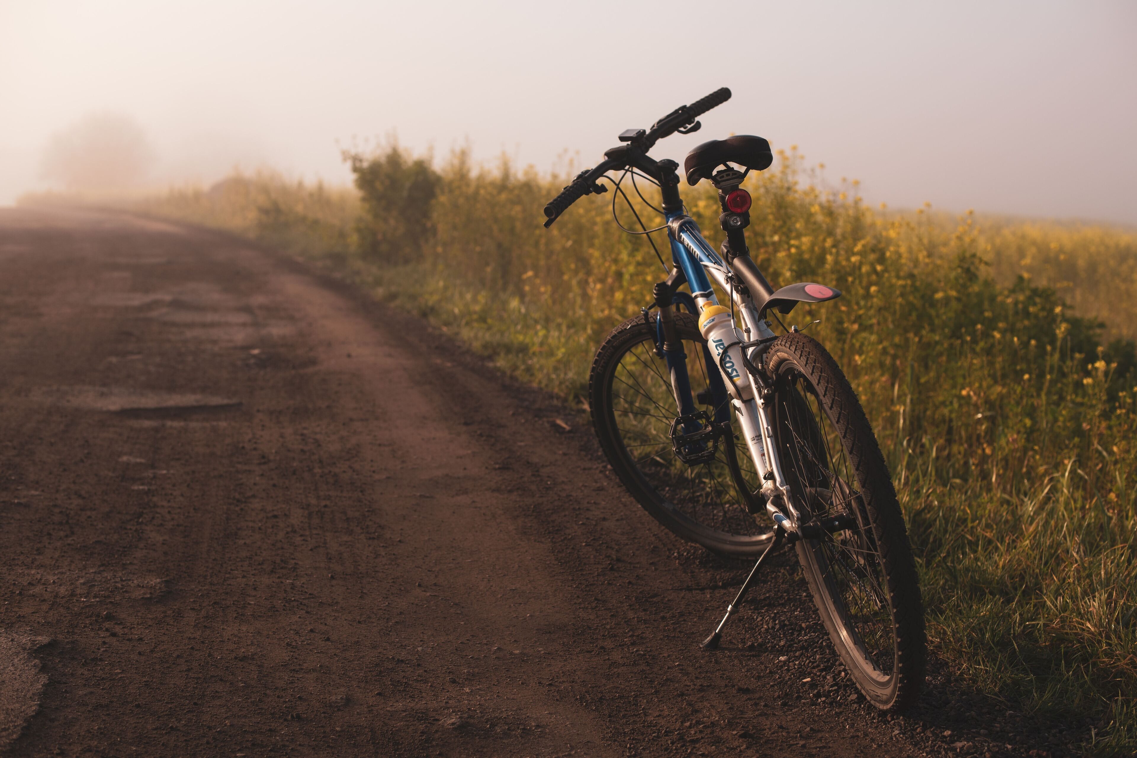A mountain bike parked on a dirt road with a rural landscape in the background.