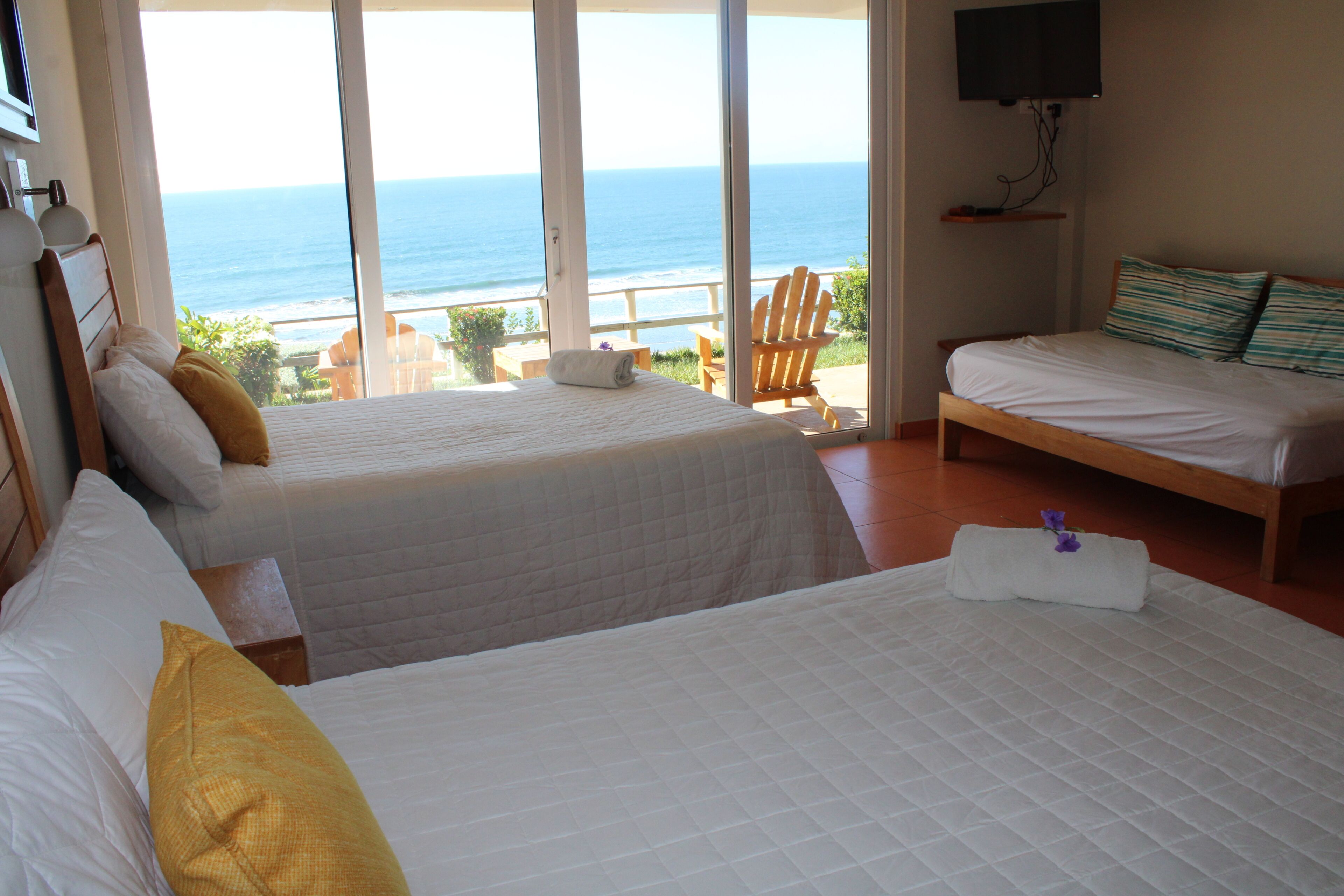 A hotel room with two beds, a TV, and a balcony with a view of the ocean.