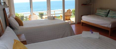 A hotel room with two beds, a TV, and a balcony with a view of the ocean.