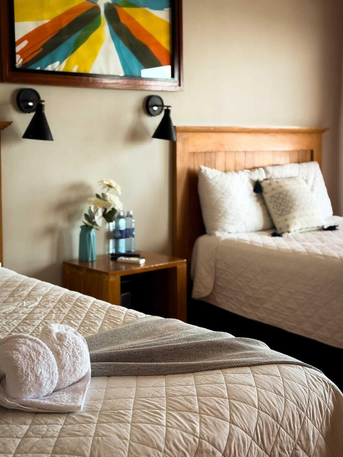 Ein Hotelzimmer mit zwei Betten, einem Nachttisch mit Blumenvase und einem Bild an der Wand.