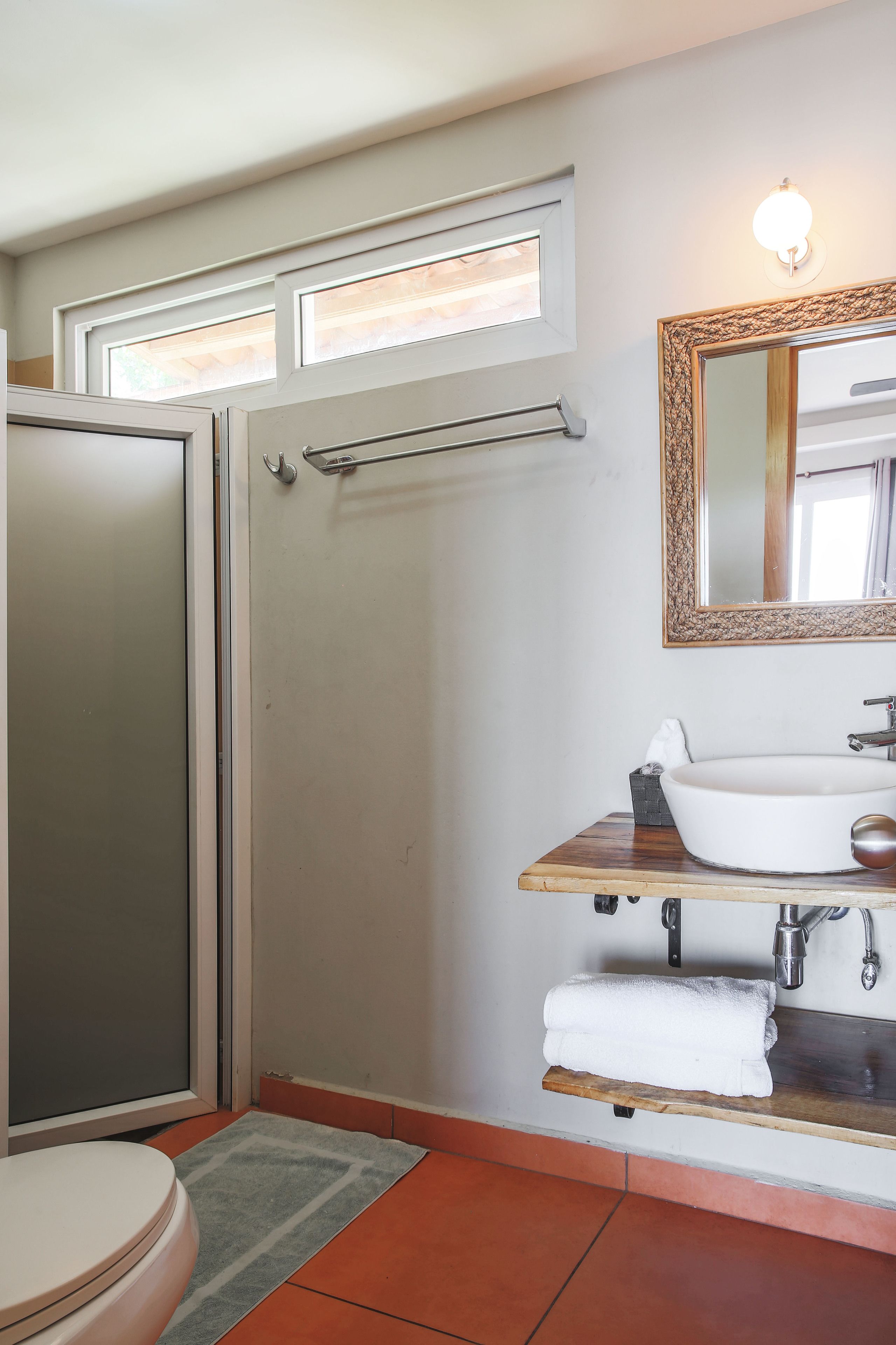 A bathroom with a glass shower door, a white sink, a mirror with a decorative frame, and a towel rack.