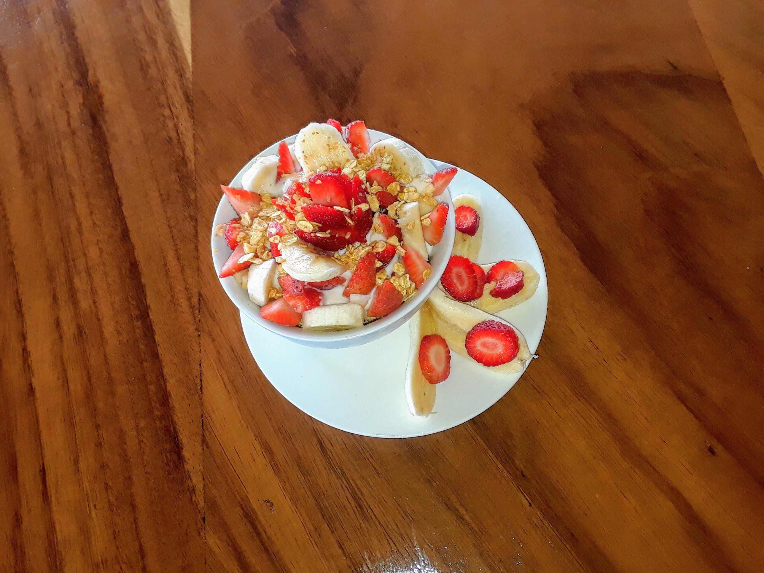 Un tazón de ensalada de frutas con fresas y plátanos sobre un plato blanco.