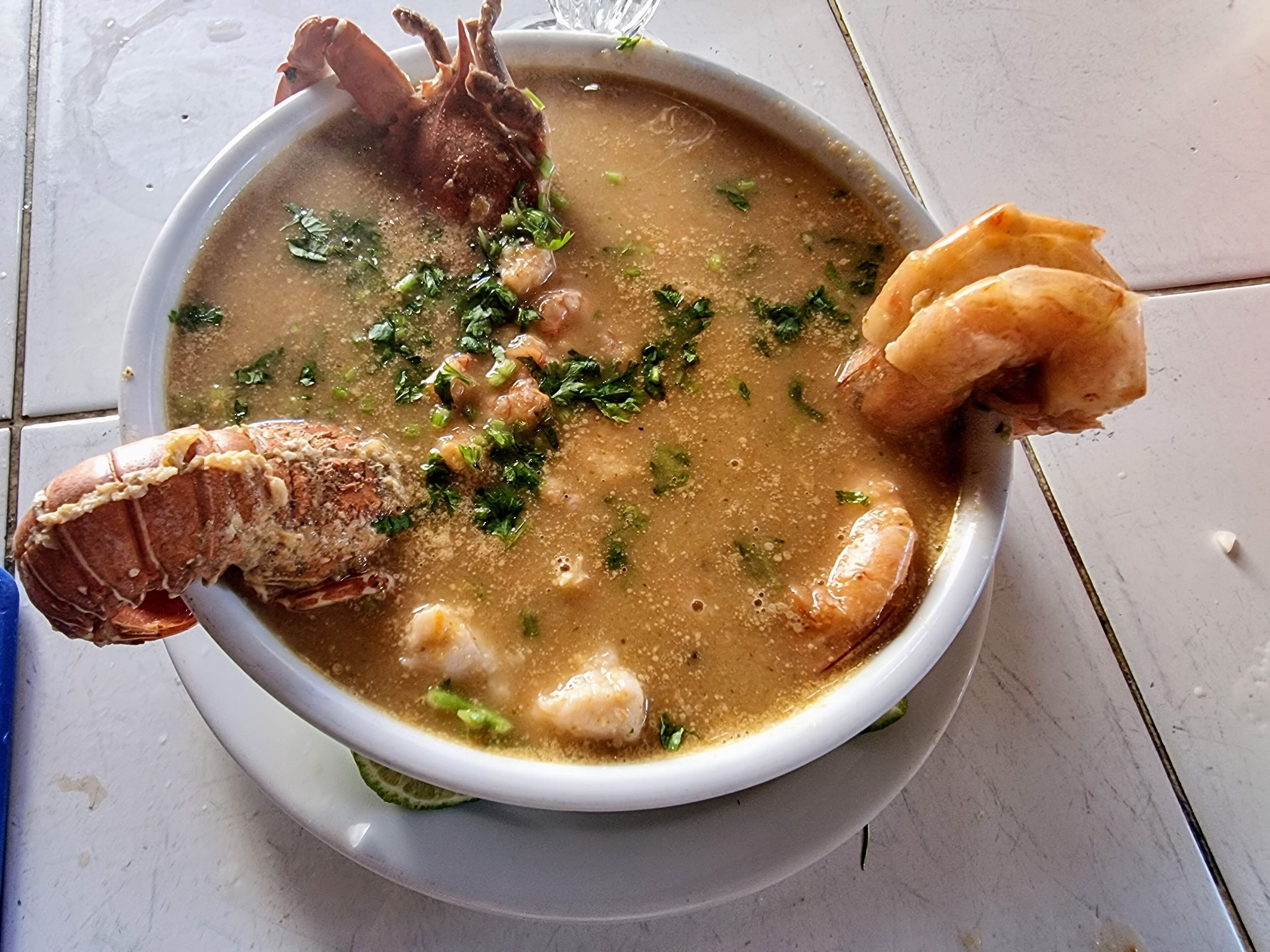 Un bol de soupe contenant divers fruits de mer et herbes aromatiques.