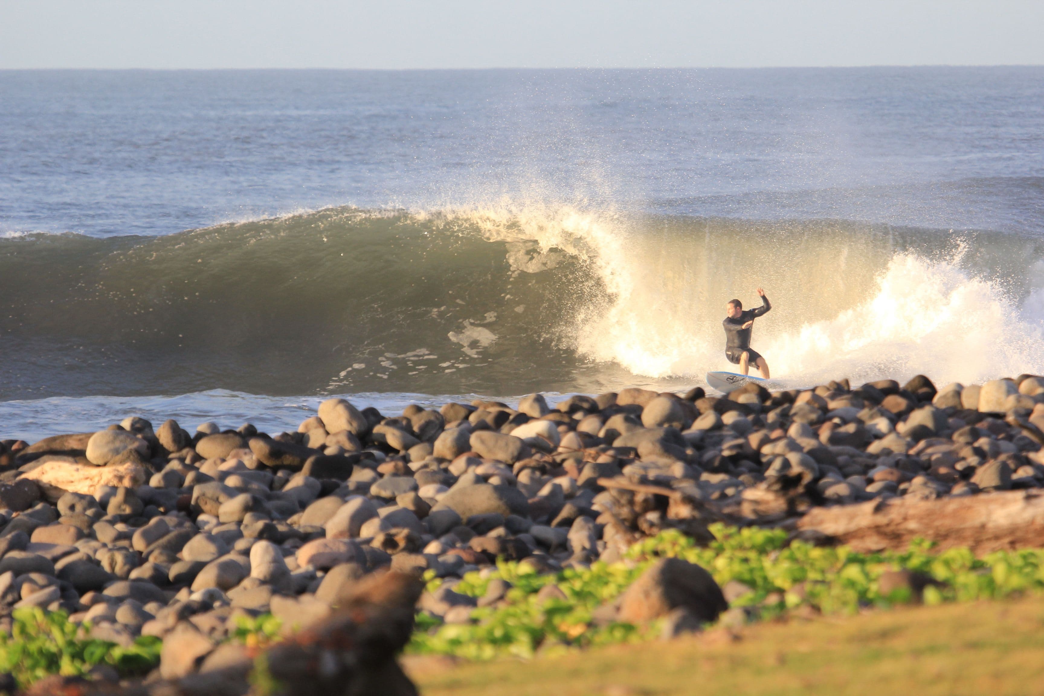 A surfer riding a wave near a rocky shoreline.