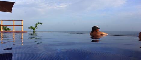 A pool with a clear view of the ocean and a palm tree.