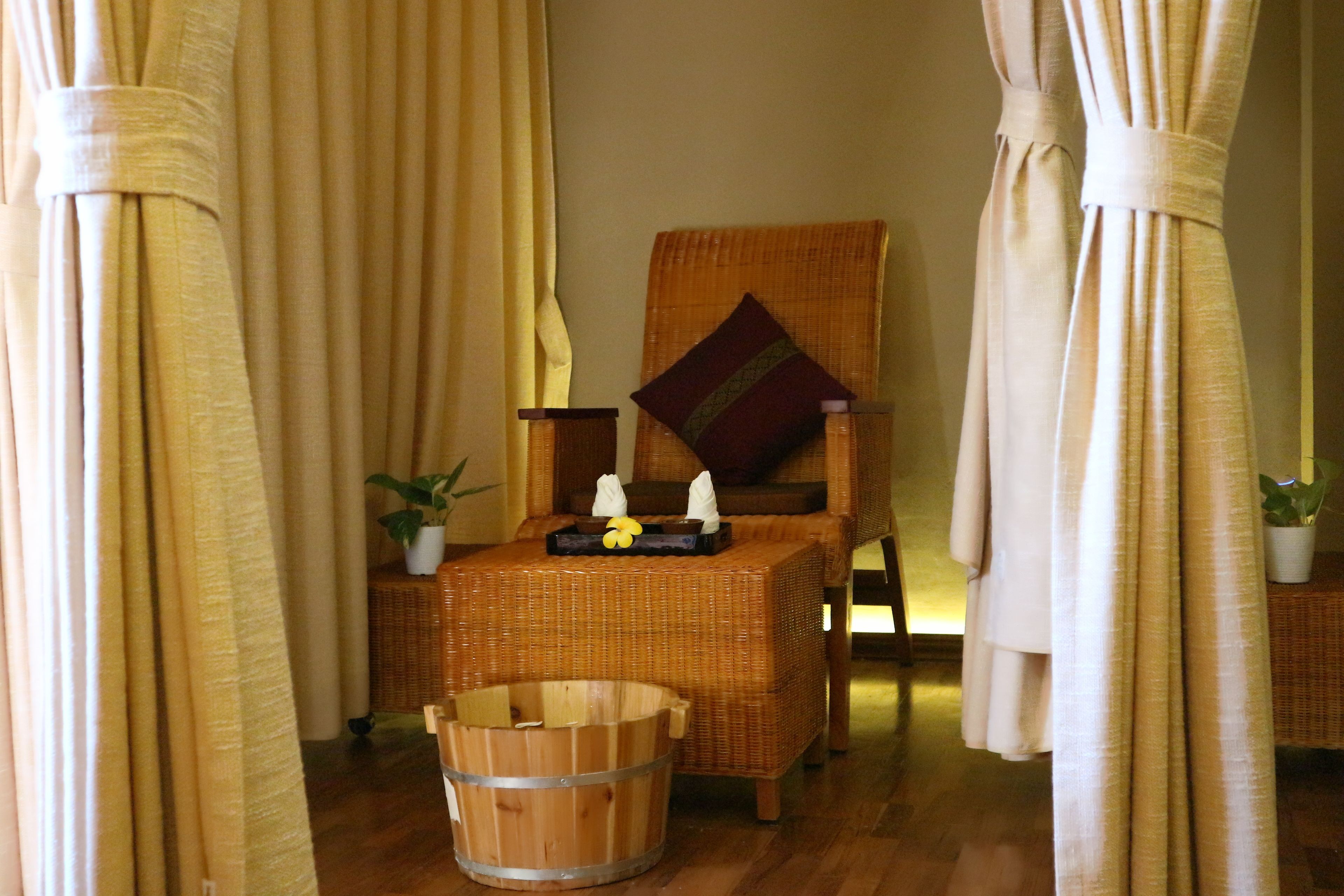 Una habitación con una silla de mimbre, un cubo de madera y una mesita con una planta y velas.
