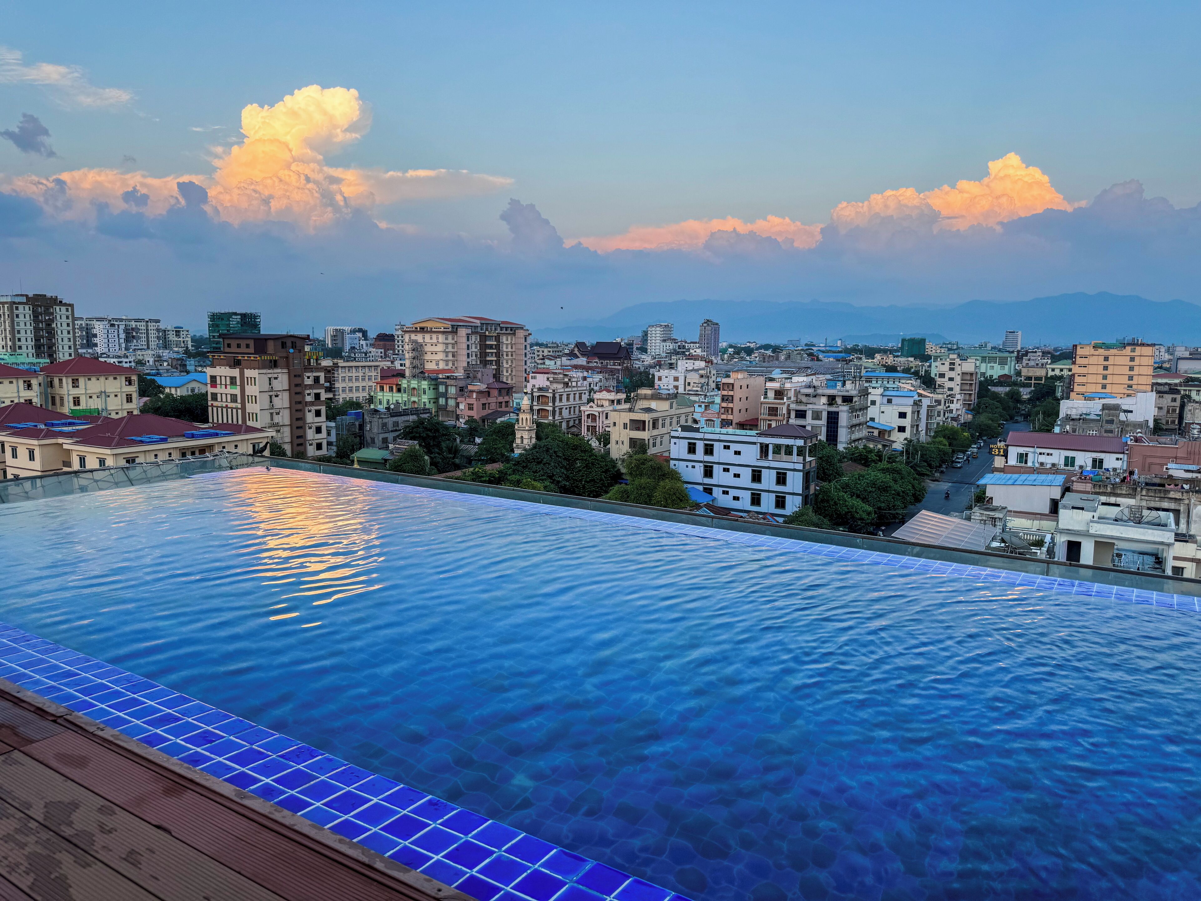 Una piscina infinita en la azotea con vistas a un paisaje urbano, rodeada de edificios y montañas.
