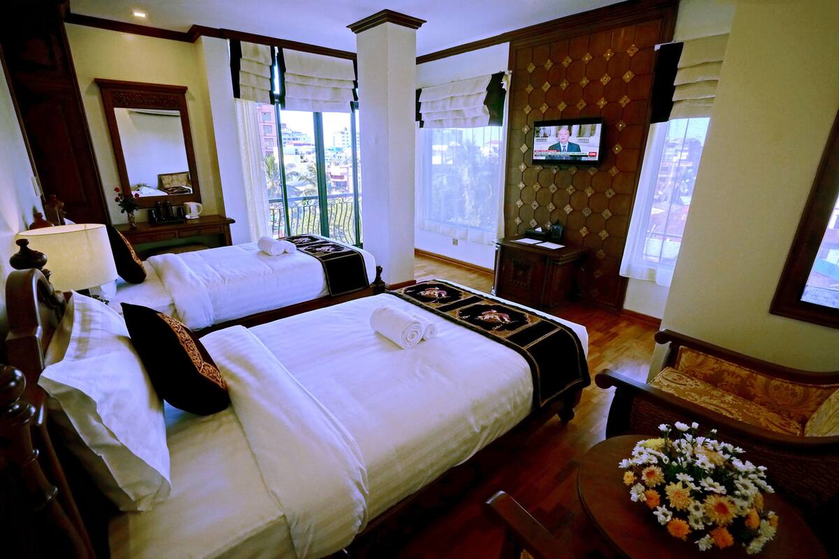 A hotel room with two beds, a TV, a balcony, and a dining area with flowers.