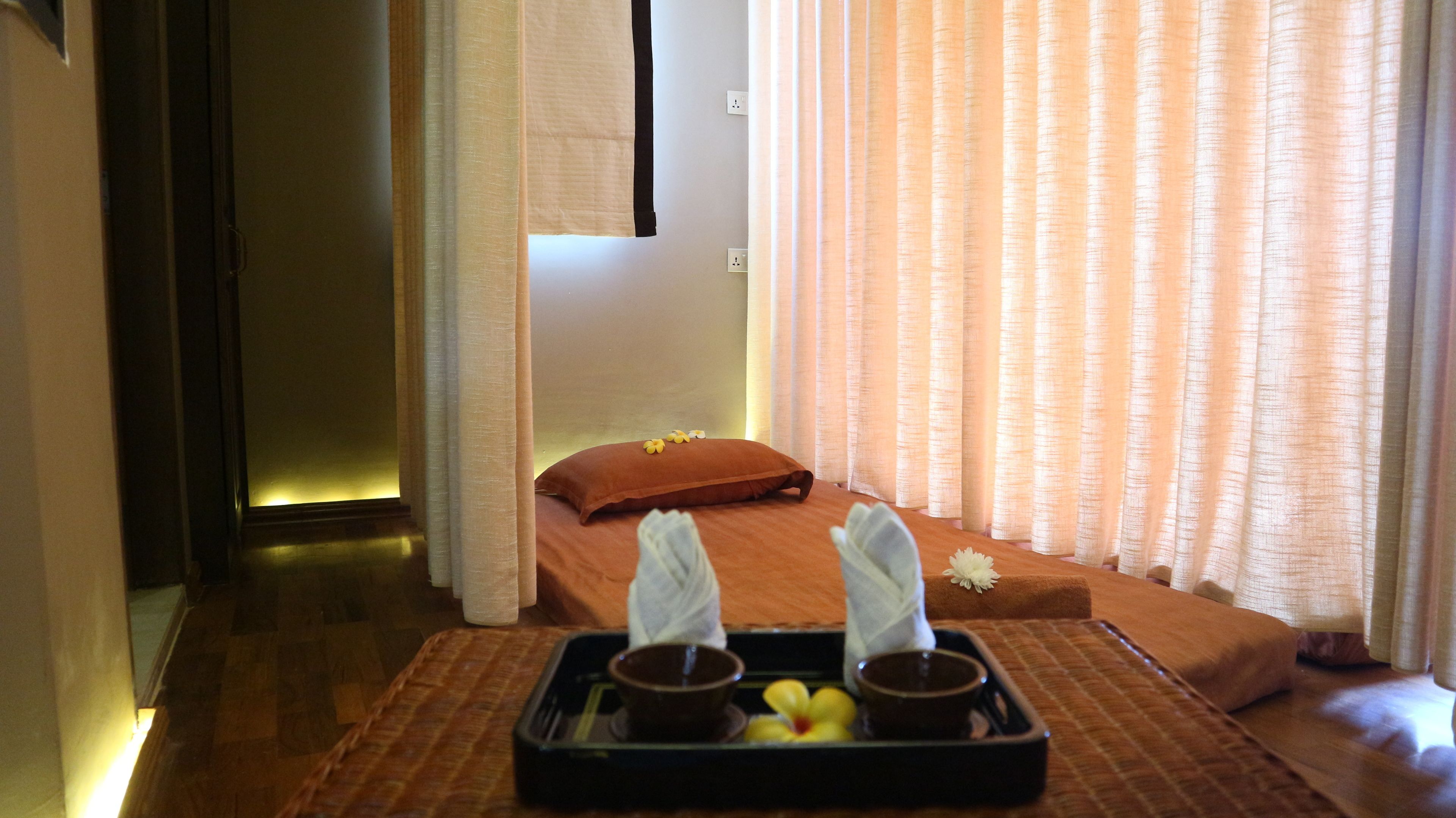 Une chambre avec un lit, un plateau contenant des bols et des fleurs, et une fenêtre avec des rideaux.