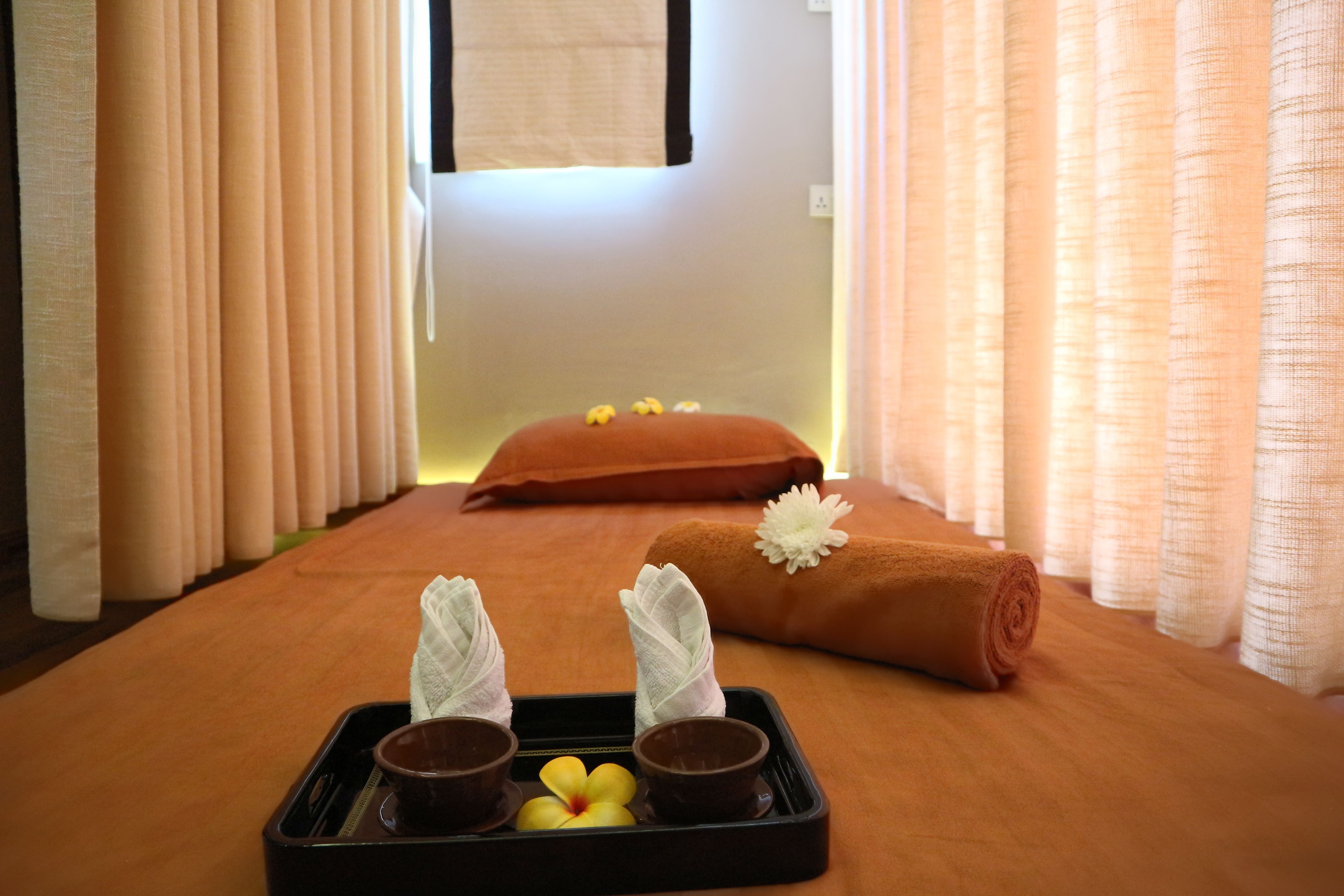 Une salle de massage équipée d’un lit en bois, de serviettes et d’un plateau sur lequel se trouvent une fleur et deux bols.