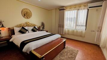A bedroom with a large bed, a bench, a decorative wall piece, and a window with curtains.