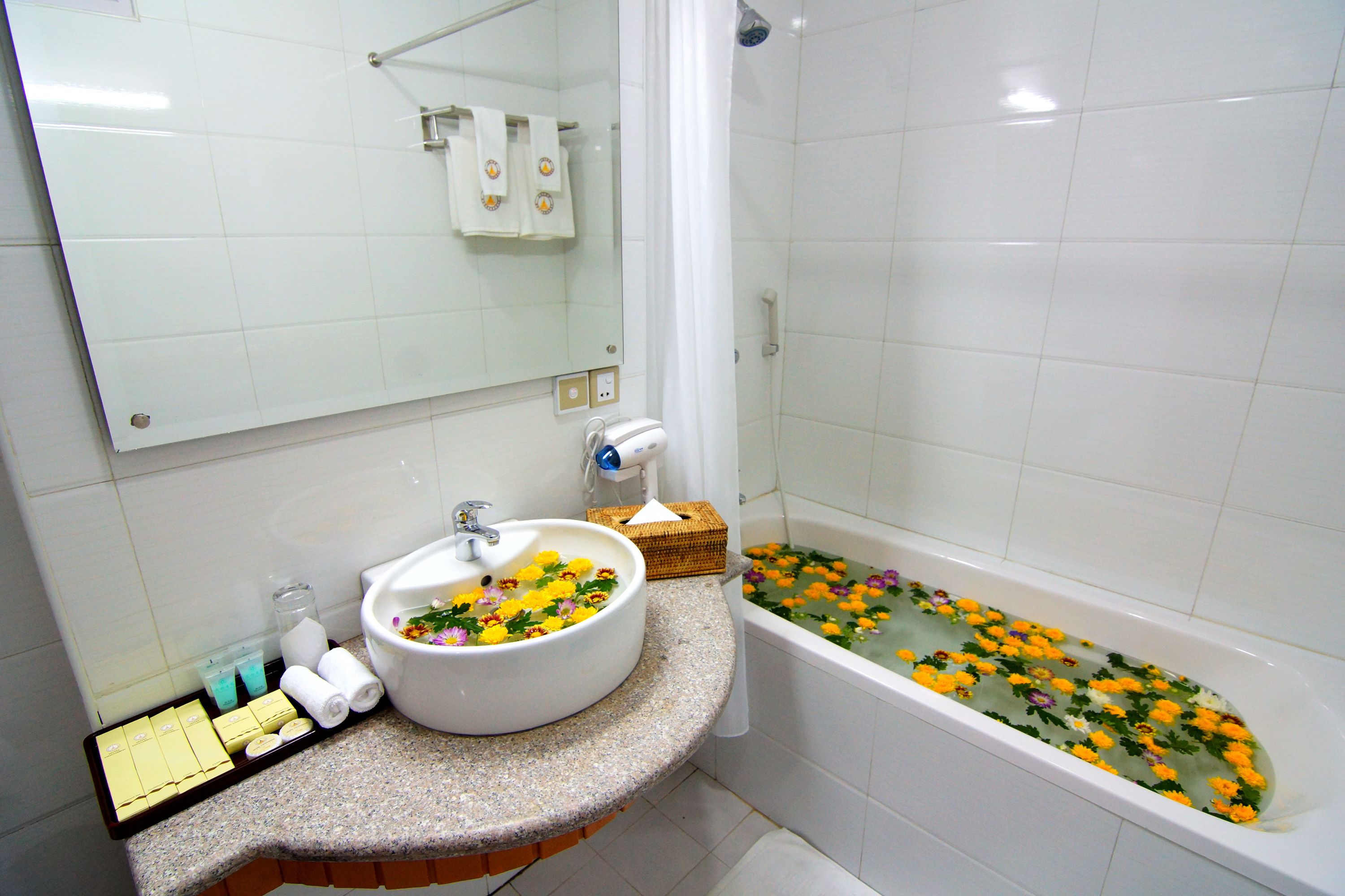 Un baño con lavabo, espejo y bañera llena de flores.