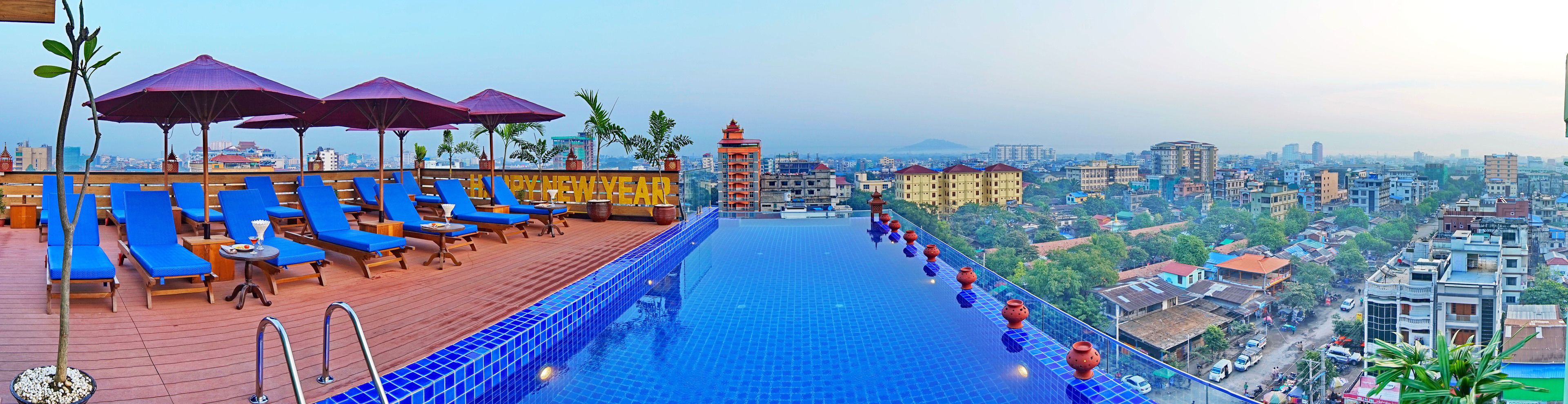 A rooftop pool with blue-tiled floor, lounge chairs, and umbrellas.
