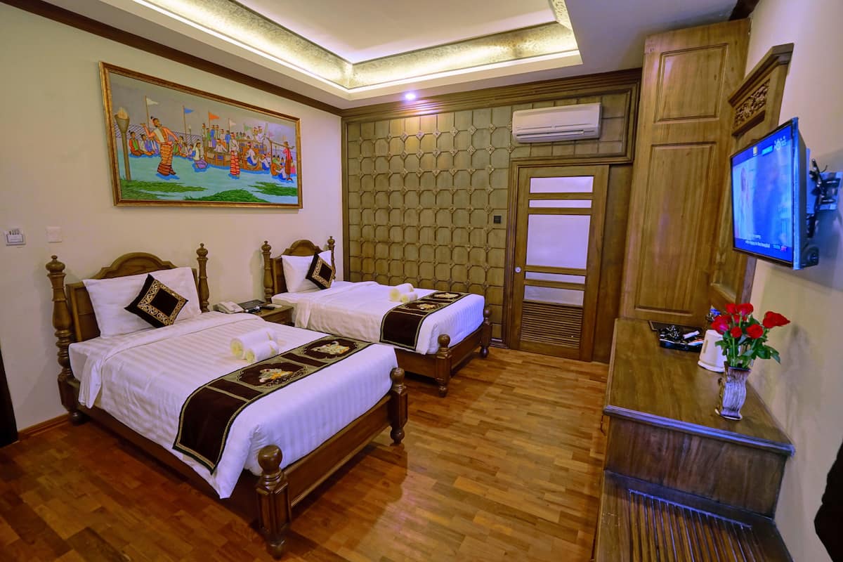 A hotel room with two wooden beds, a painting on the wall, a television on a wooden cabinet, and a wooden floor.