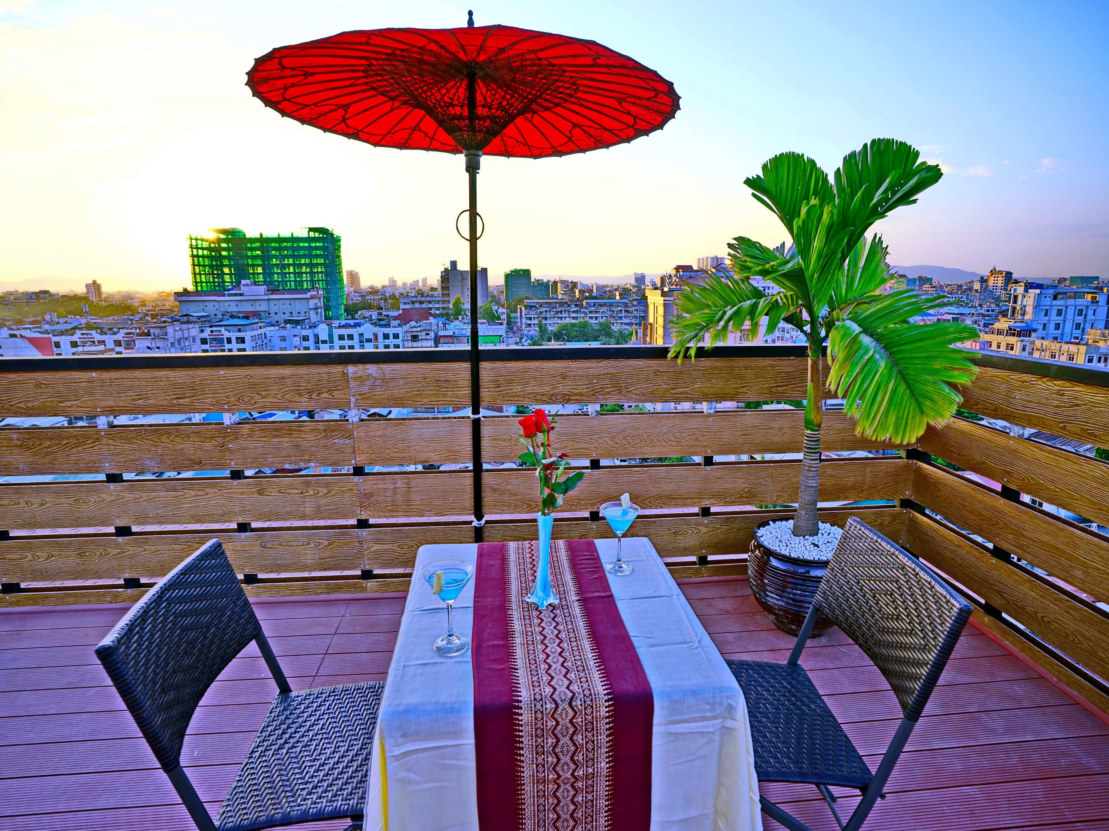 Terraza en la azotea con una mesa para dos, una sombrilla roja y vistas panorámicas de la ciudad.
