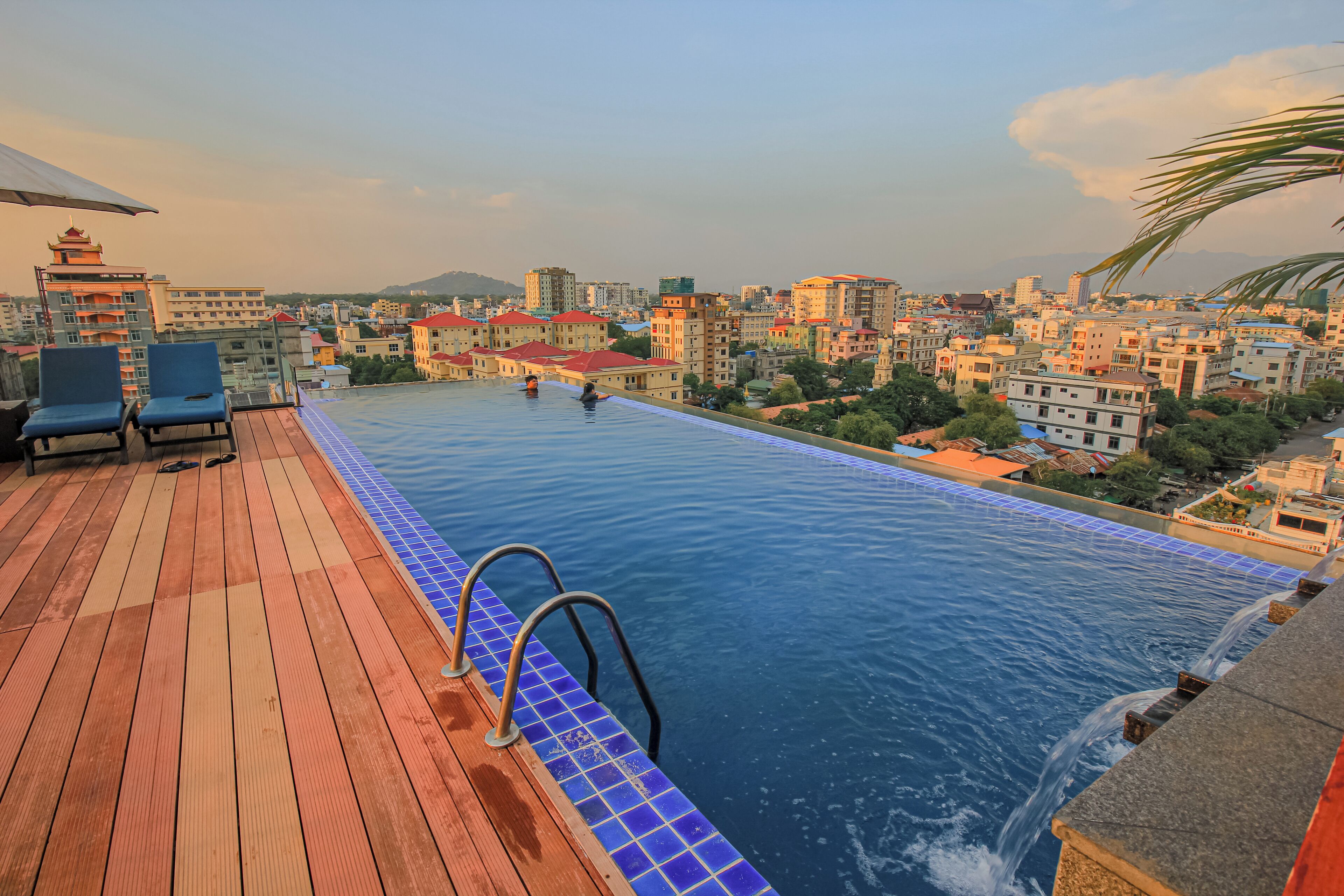 A rooftop swimming pool with a wooden deck and a cityscape view.