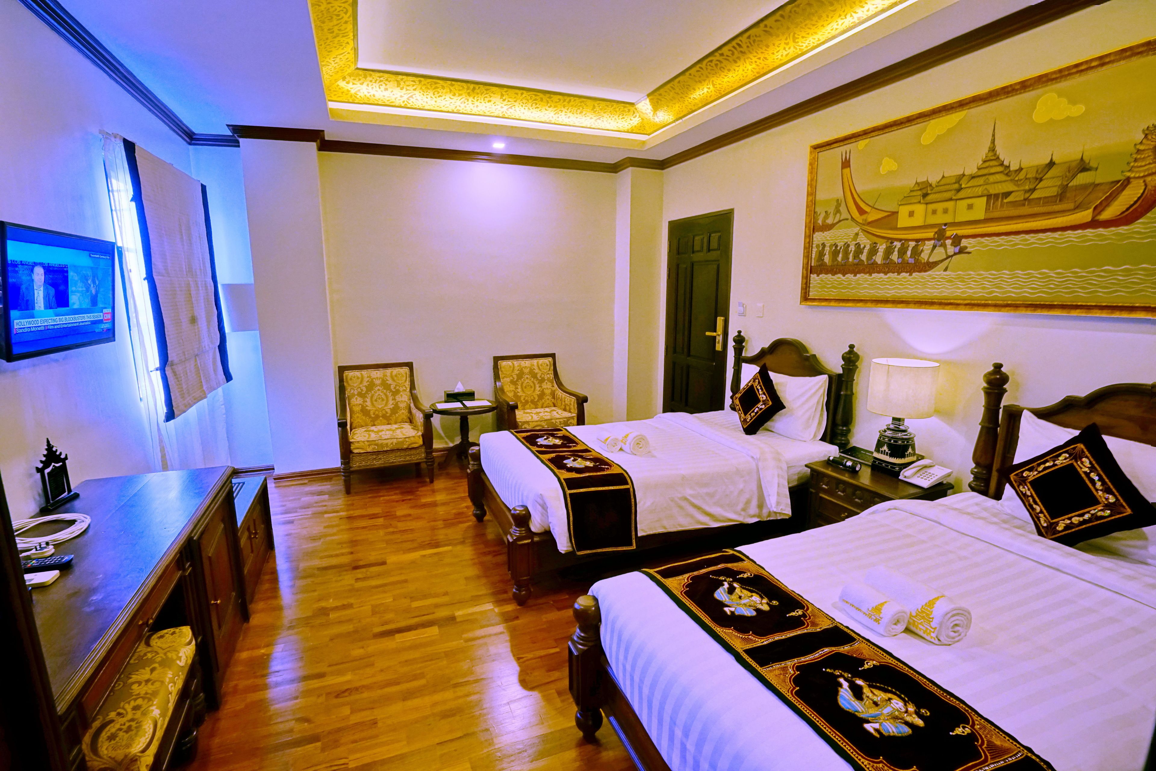 A hotel room with two beds, a desk, a chair, a television, and a painting on the wall.
