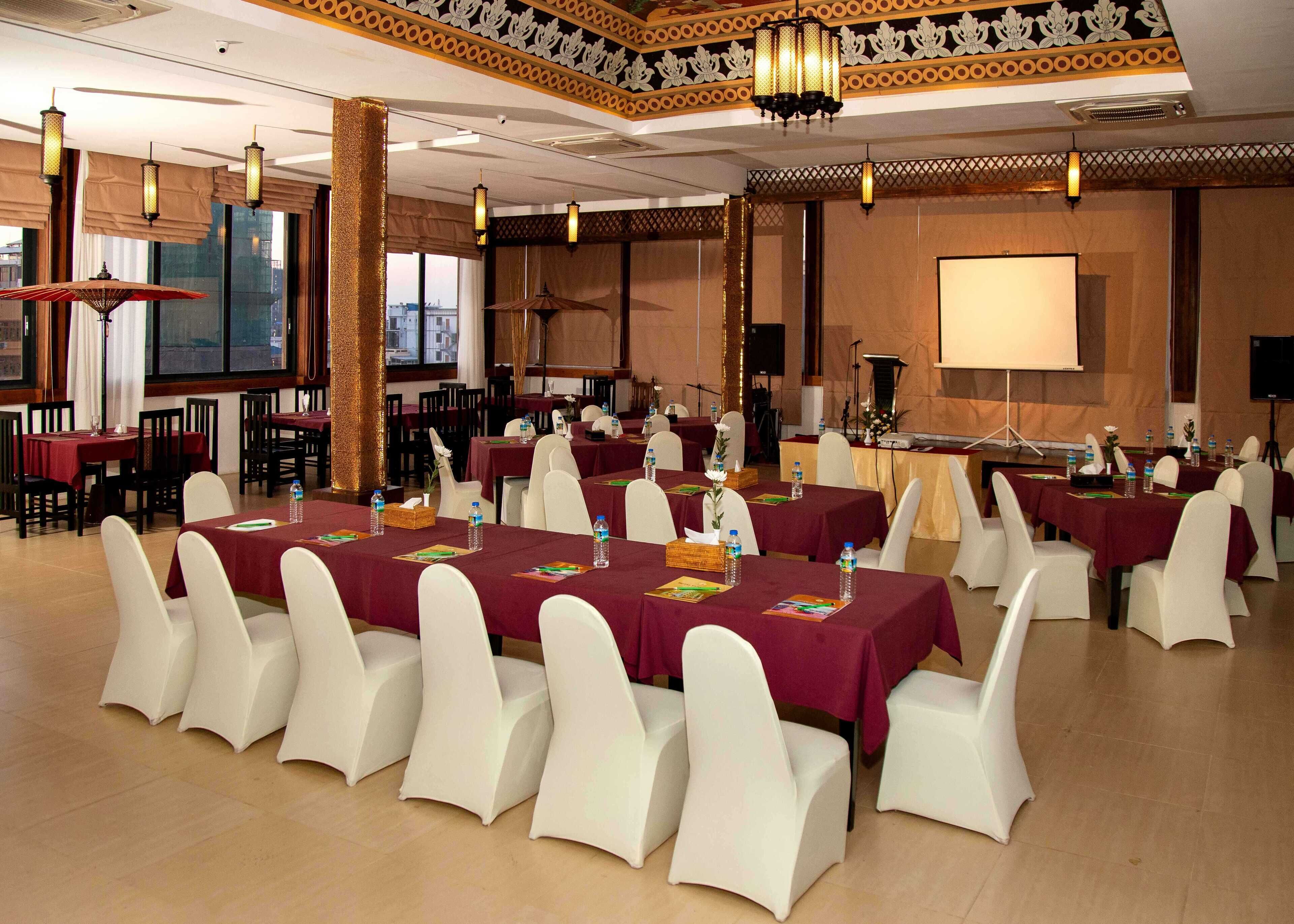 A conference room with tables set for a meeting, white chairs, and a projector screen.
