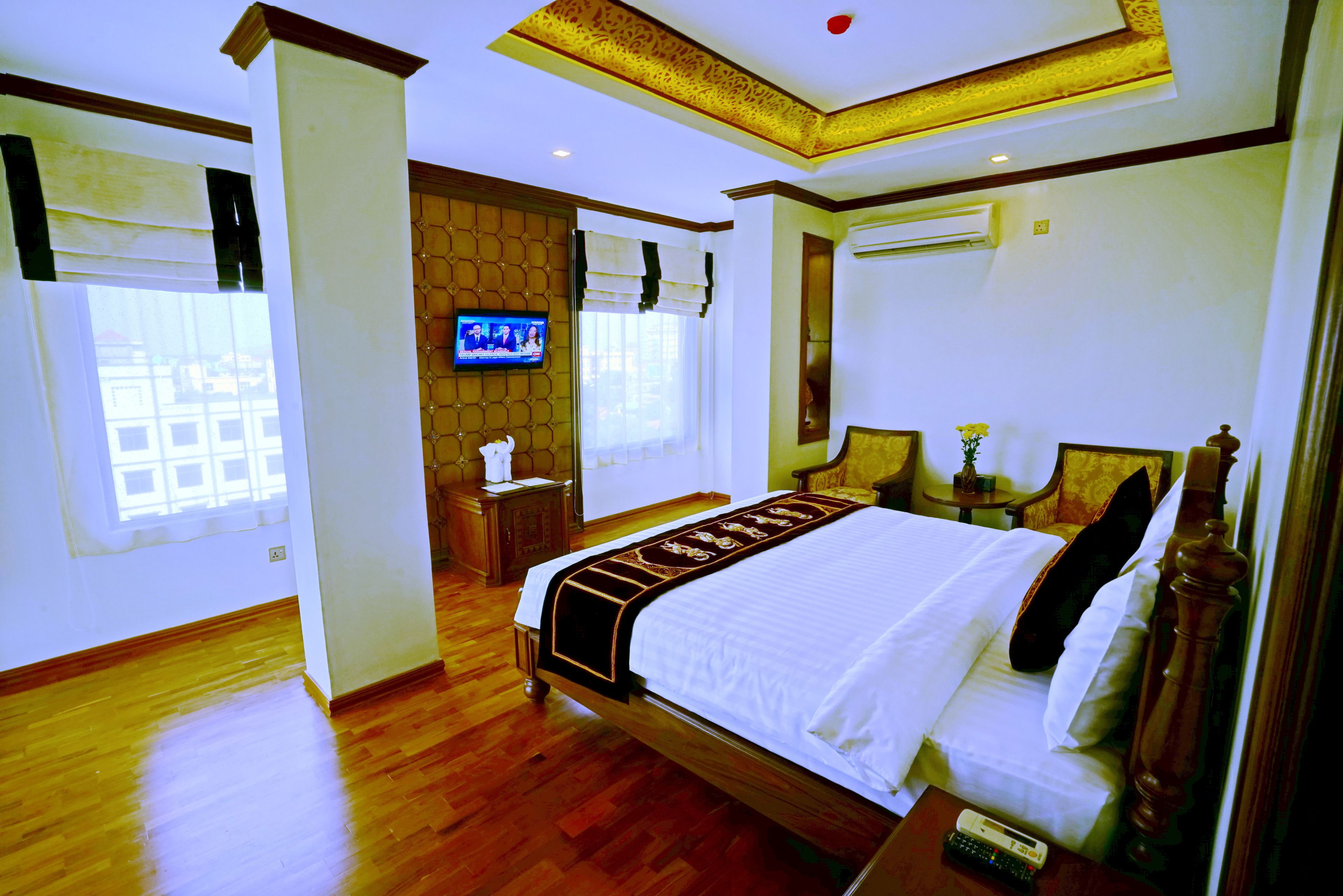 A hotel room with a large bed, a television, a wooden floor, and a window with blinds.