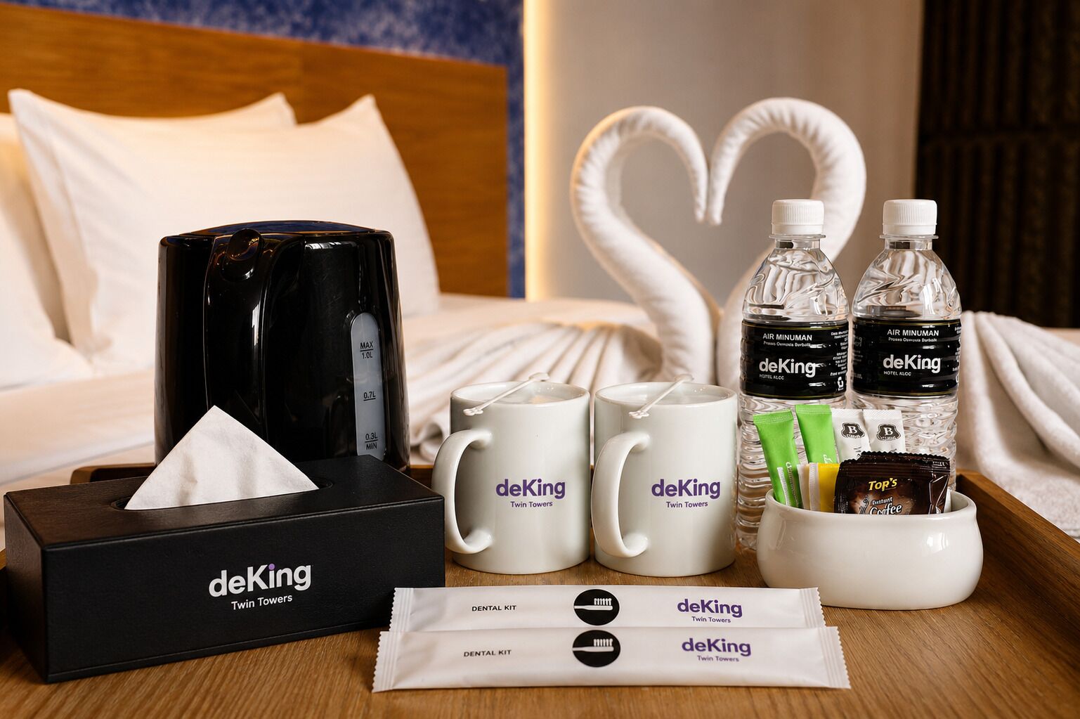 Une chambre d’hôtel comprenant un lit, une table de chevet avec une machine à café, deux tasses blanches, deux bouteilles d’eau, un porte-brosses à dents avec des brosses à dents, du dentifrice et du fil dentaire.