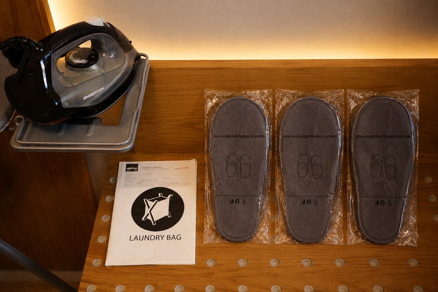 A wooden surface with a shoe dryer, three pairs of slippers, and a laundry bag.