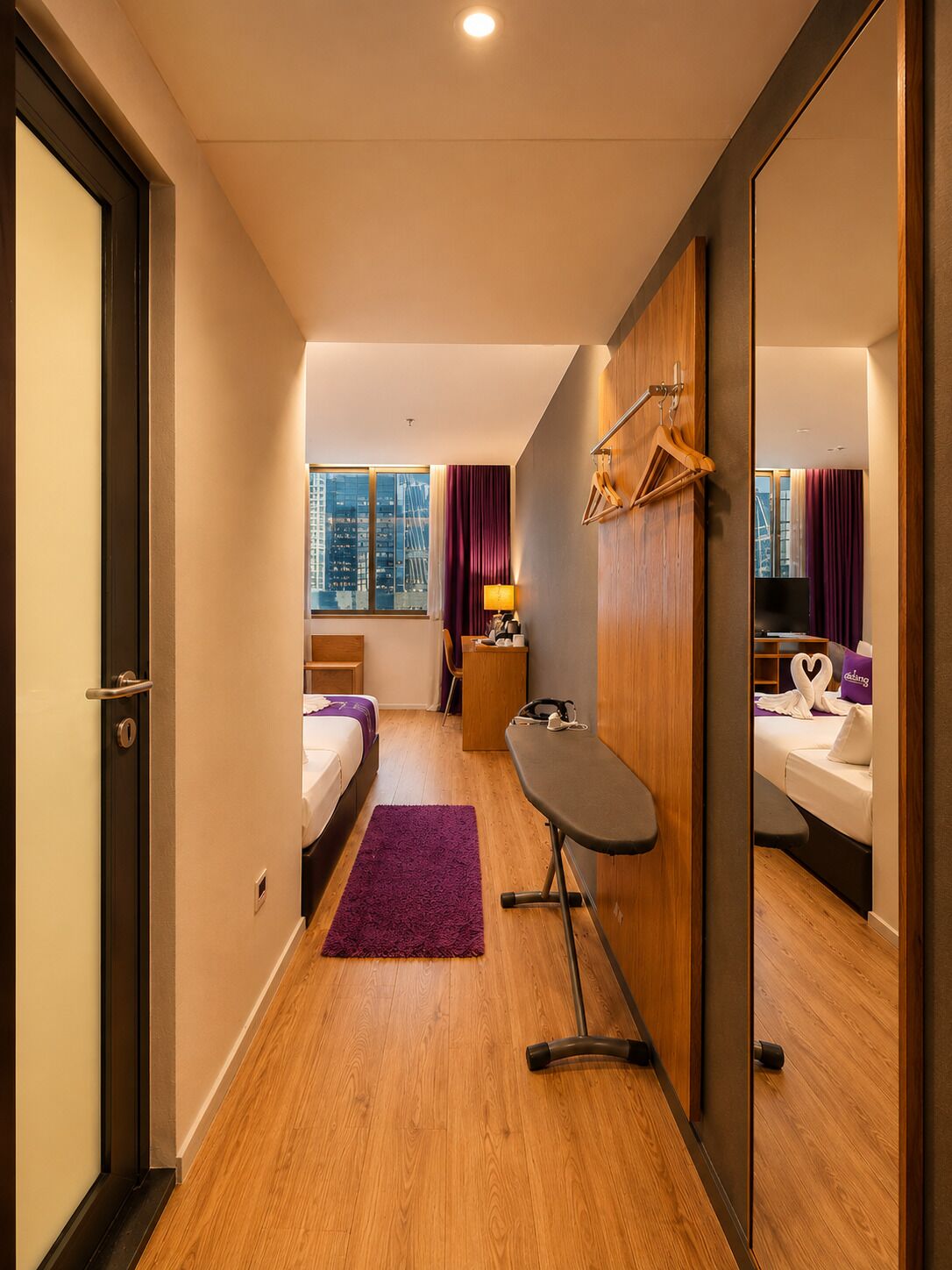 A hotel room with a bed, a desk, a mirror, a window with curtains, and a city view.