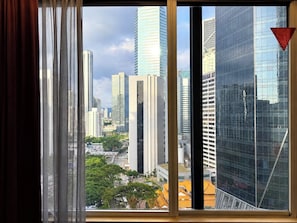 A cityscape through a window with curtains, featuring modern high-rise buildings and a mix of architectural styles. - deKing Hotel Twin Towers KLCC (Kuala Lumpur)